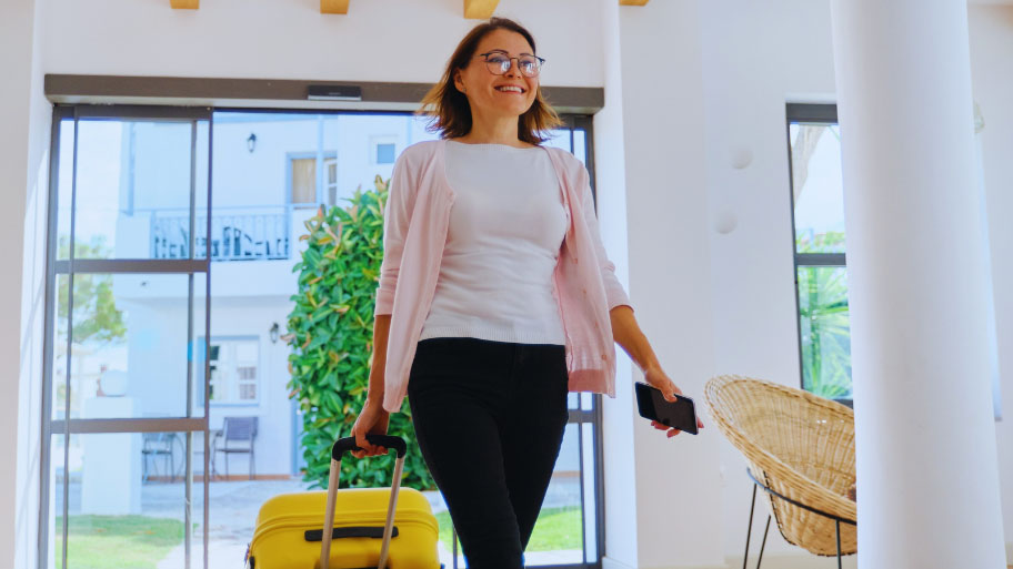 Mature Traveling Woman Entering Hotel with Suitcase